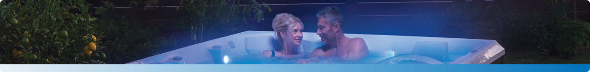 A couple relaxing in a hot tub illuminated by blue lights, surrounded by nature.