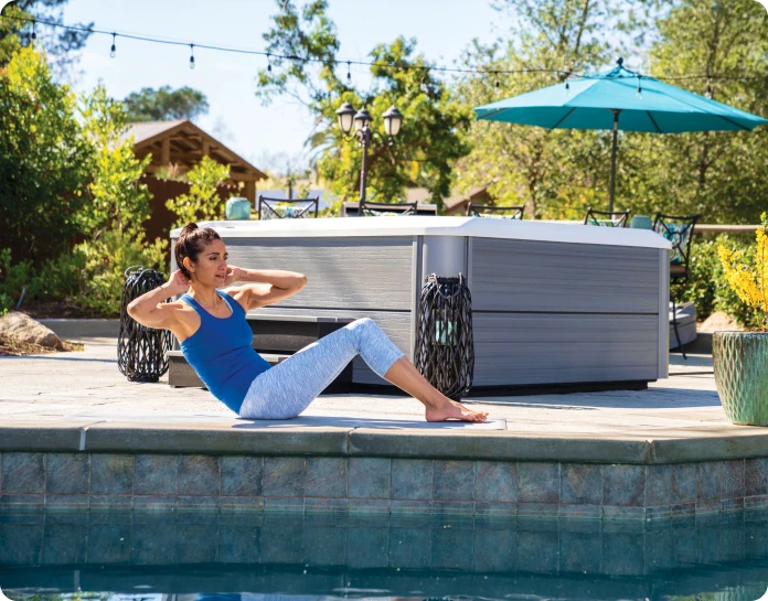 A woman exercising near a hot tub, enjoying the view of a sparkling pool with a relaxation zone in the background.