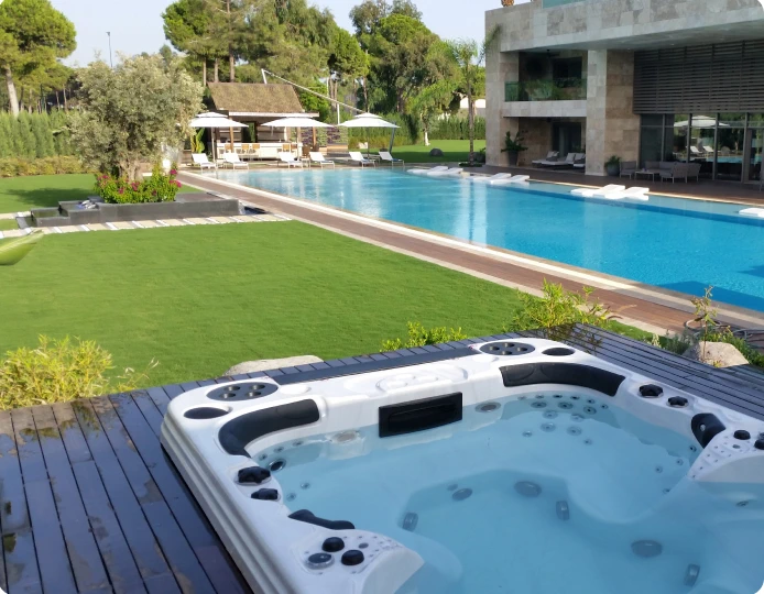 A hot tub near a sparkling swimming pool, with a relaxing zone and a building in the background.